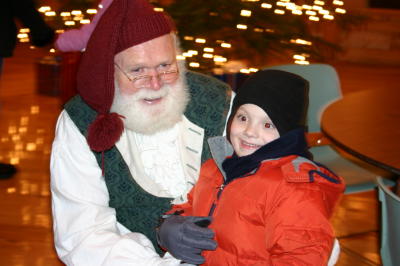 A little boy with a red coat and black hat sitting on Santas lap